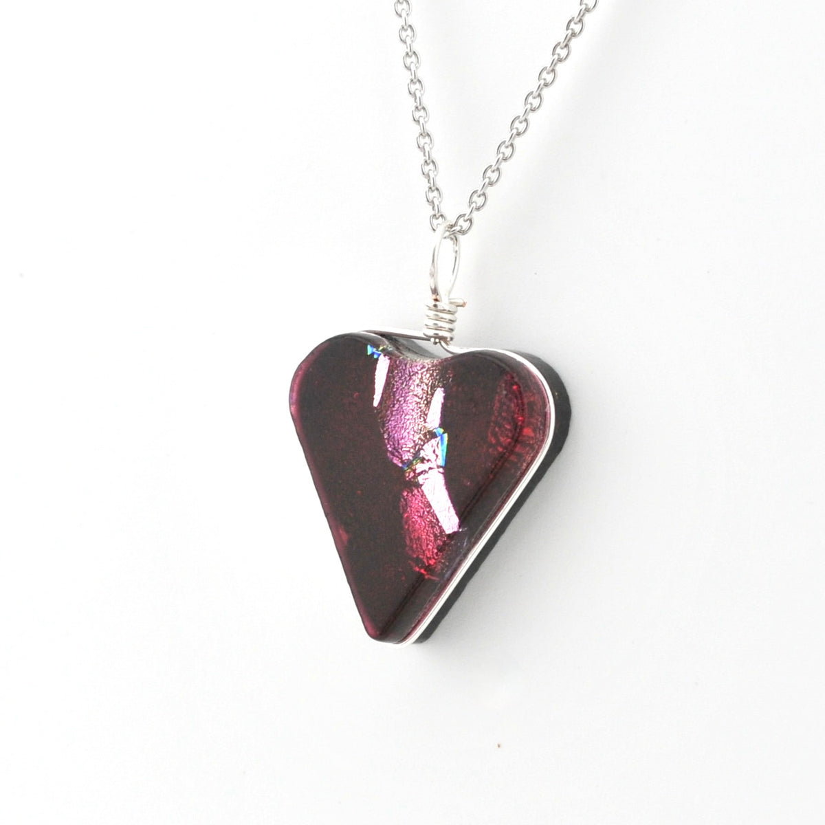 A heart-shaped glass pendant necklace with an iridescent dark red and magenta finish, suspended from a silver chain on a white background.