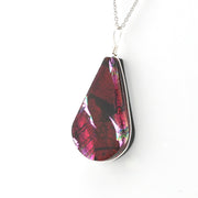 A teardrop-shaped pendant necklace featuring a glossy, iridescent red and magenta dichroic glass with silver-toned metal edges and a silver chain, shown against a plain white background.