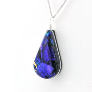 A teardrop-shaped pendant necklace featuring a vibrant blue and purple dichroic glass with gold flecks, set in a silver bezel with a silver chain.