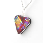 A heart-shaped glass pendant necklace with an iridescent, multicolored pattern of red, purple, blue, and yellow, suspended from a silver chain on a white background.