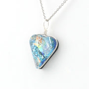 A silver pendant necklace featuring a triangular glass piece with a vibrant blue, green, and orange iridescent pattern, suspended from a silver chain against a plain white background.