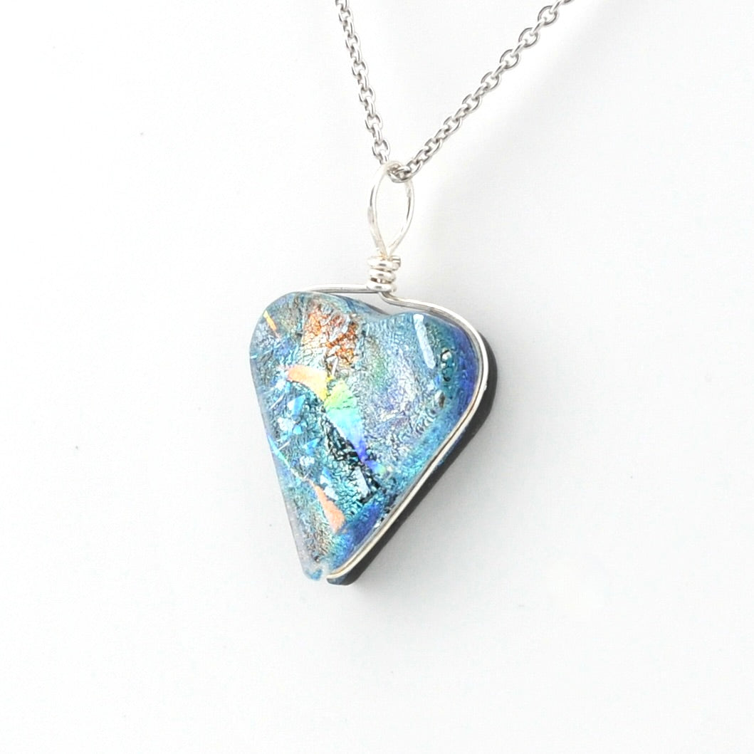 A silver pendant necklace featuring a triangular glass piece with a vibrant blue, green, and orange iridescent pattern, suspended from a silver chain against a plain white background.