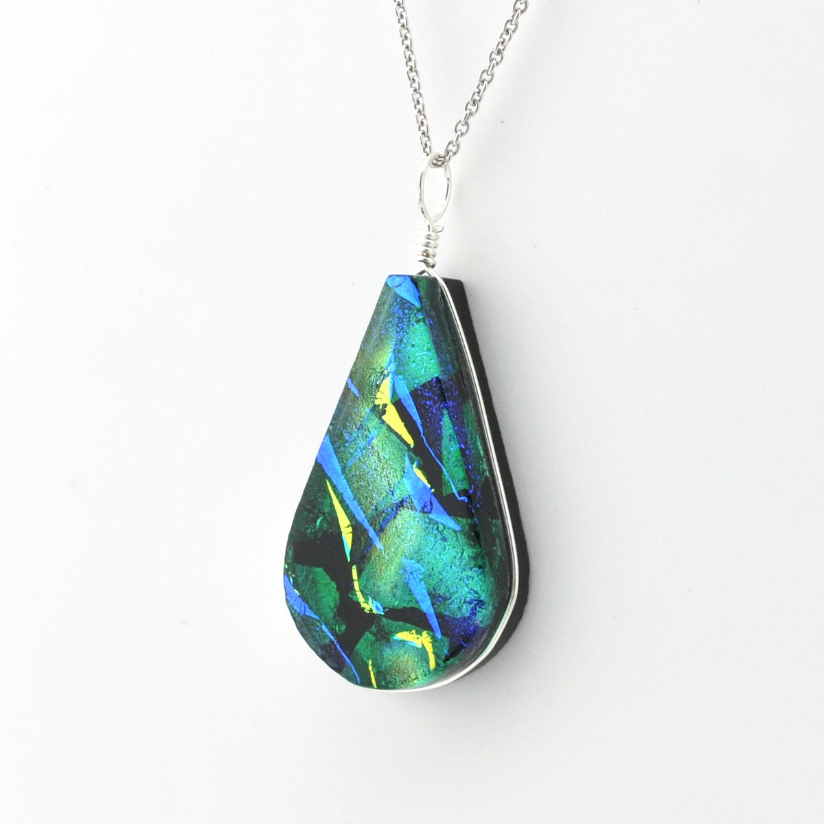 A teardrop-shaped pendant necklace featuring a colorful abstract pattern of green, blue, and yellow on a black background, suspended from a silver chain against a plain white background.