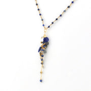 A gold chain necklace featuring a dangle pendant made of deep blue lapis gemstone chips and small blue beads, shown against a plain white background.