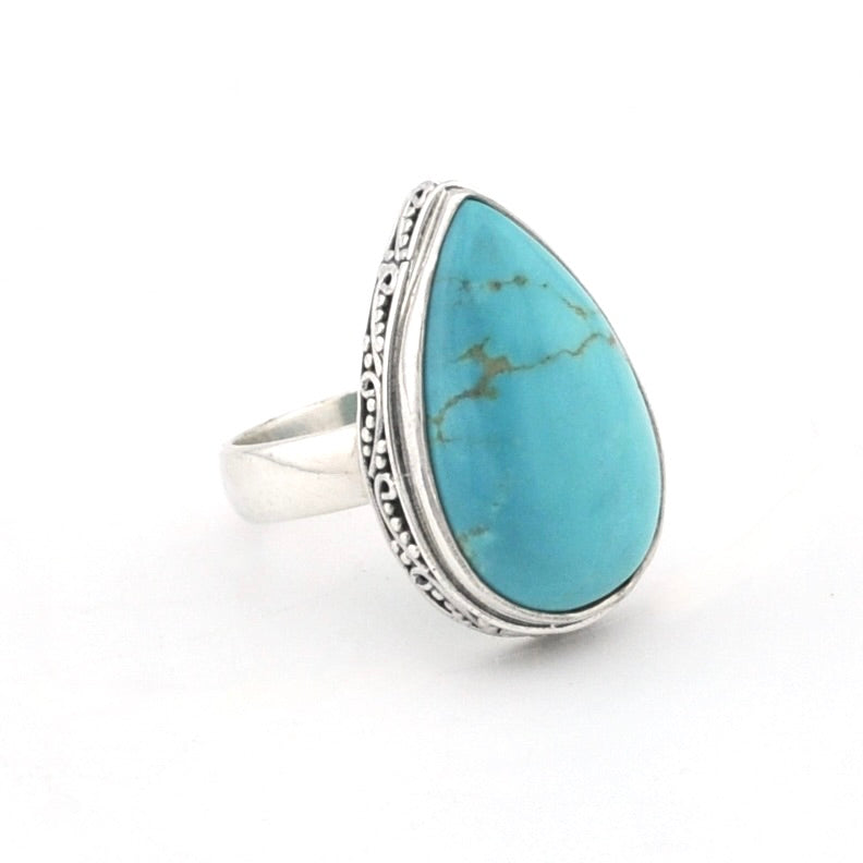 A silver ring featuring a large, teardrop-shaped turquoise stone with natural matrix veining, set in a silver bezel with a decorative, scalloped border.