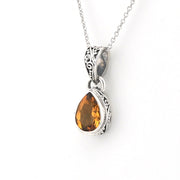 A silver pendant necklace featuring a teardrop-shaped citrine gemstone in an ornate silver bezel setting, suspended from a delicate silver chain against a plain white background.