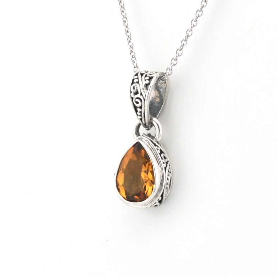 A silver pendant necklace featuring a teardrop-shaped citrine gemstone in an ornate silver bezel setting, suspended from a delicate silver chain against a plain white background.