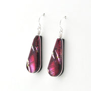 A pair of teardrop-shaped dangle earrings made from dichroic glass in shades of magenta, purple, and pink, suspended from silver fishhook wires on a plain white background.