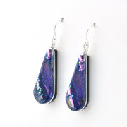 A pair of teardrop-shaped dangle earrings with iridescent purple and blue glass inlays, suspended from silver fishhook wires on a plain white background.