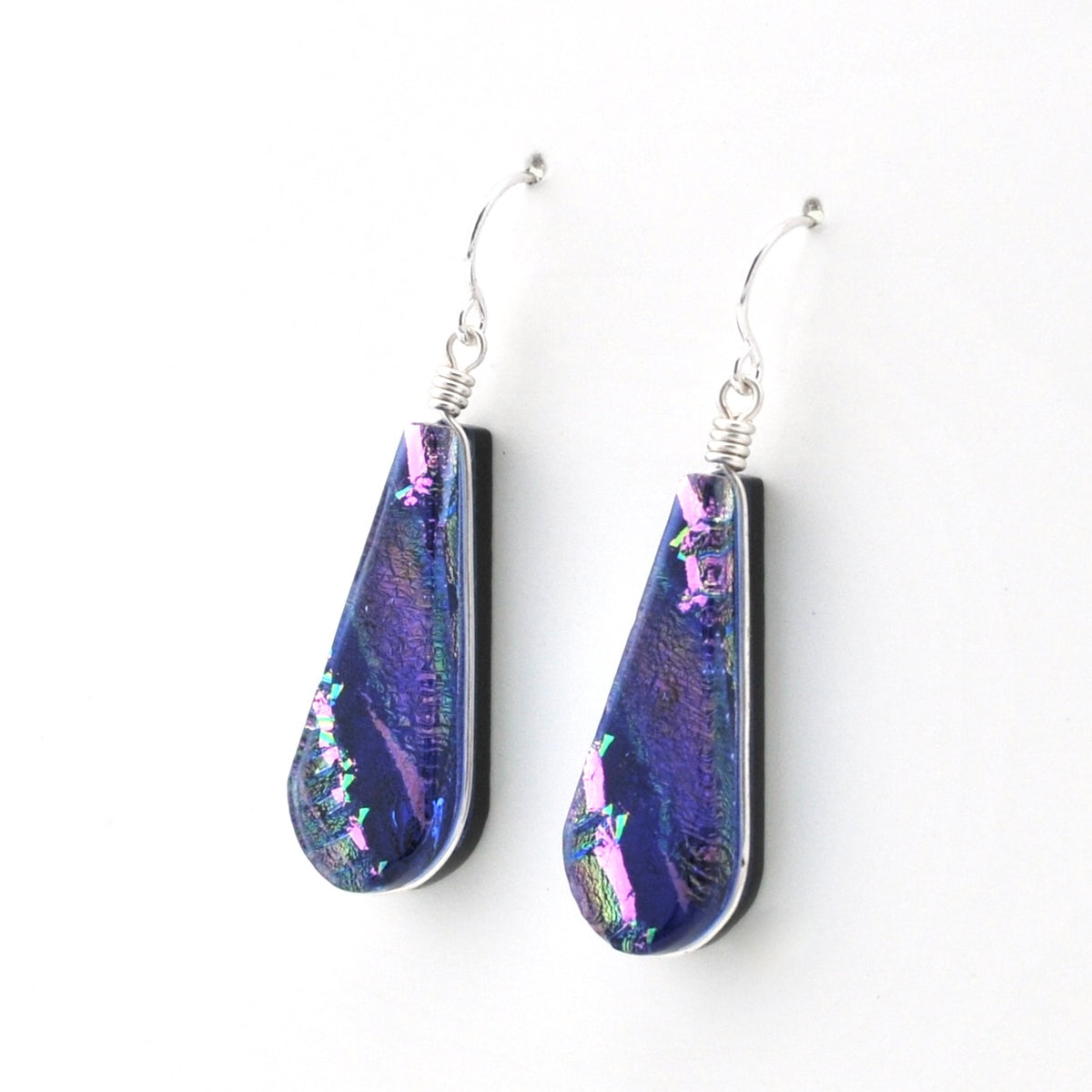 A pair of teardrop-shaped dangle earrings with iridescent purple and blue glass inlays, suspended from silver fishhook wires on a plain white background.