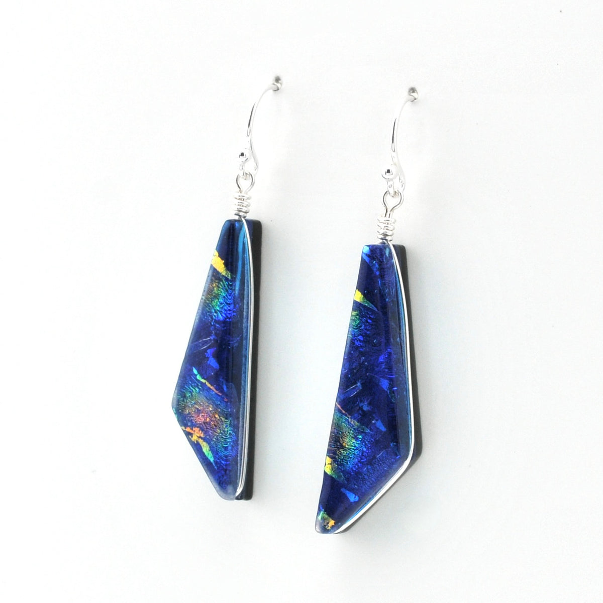 A pair of dangle earrings with irregular blue and iridescent dichroic glass pendants on silver fishhook wires, shown against a plain white background.