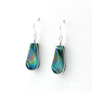 A pair of teardrop-shaped drop earrings featuring iridescent green, blue, and orange dichroic glass set in silver bezel, suspended from silver fishhook wires on a white background.