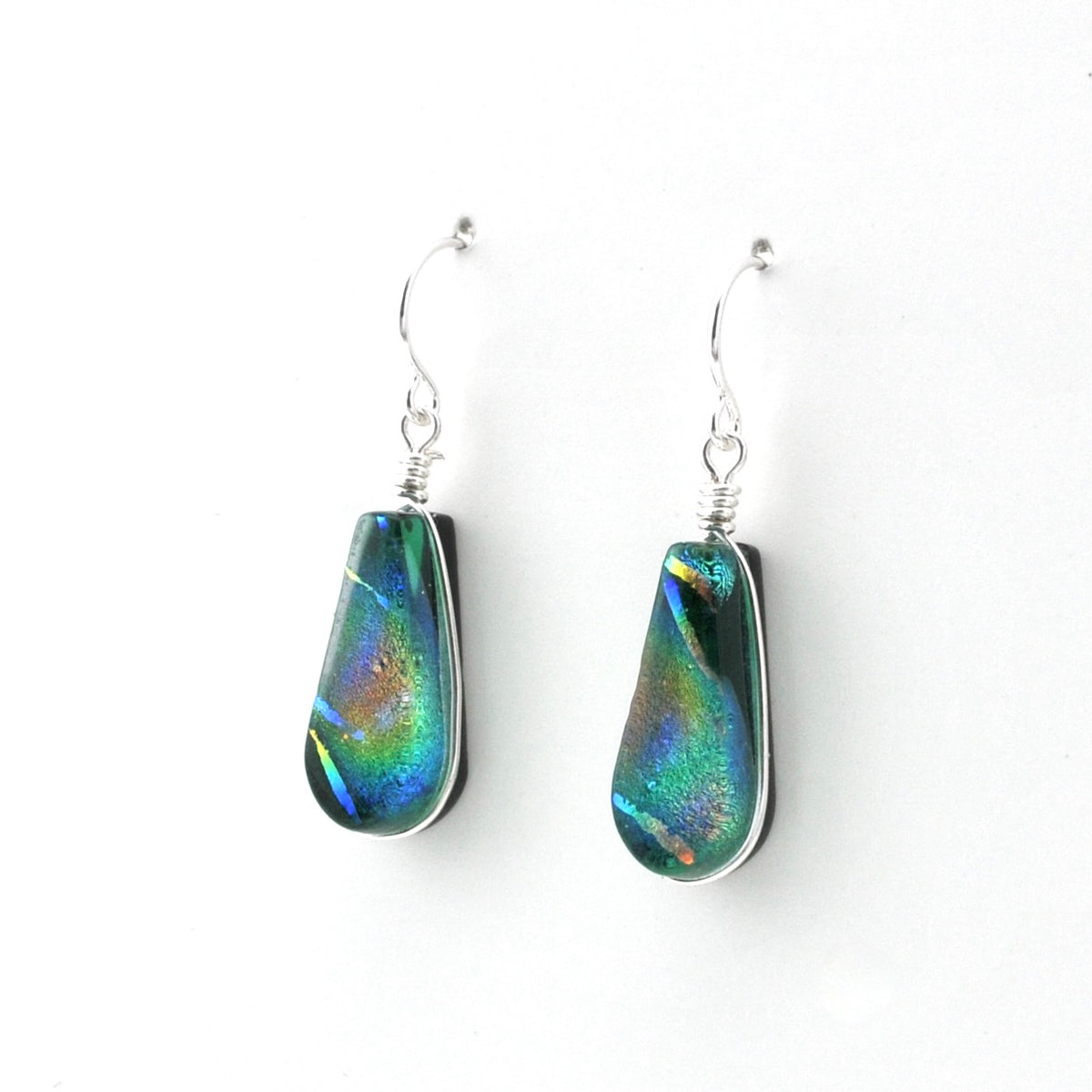 A pair of teardrop-shaped drop earrings featuring iridescent green, blue, and orange dichroic glass set in silver bezel, suspended from silver fishhook wires on a white background.
