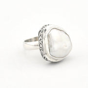 A sterling silver ring featuring a large, irregularly shaped white pearl bezel-set in an ornate, textured silver frame, shown on a plain white background.