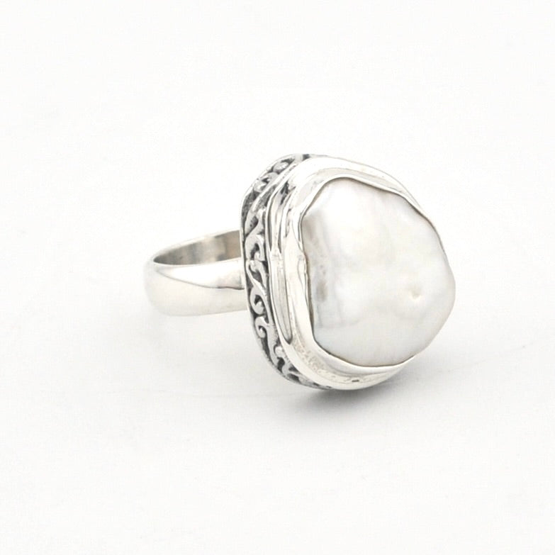 A sterling silver ring featuring a large, irregularly shaped white pearl bezel-set in an ornate, textured silver frame, shown on a plain white background.