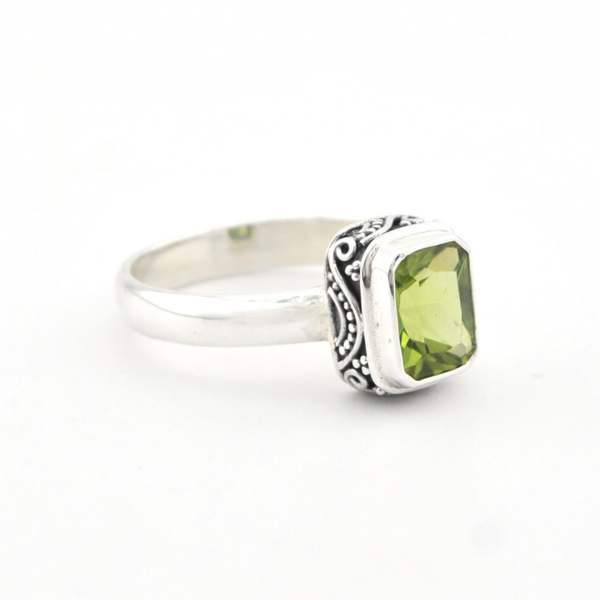 A sterling silver ring featuring a rectangular green peridot gemstone with a decorative filigree band, set against a plain white background.