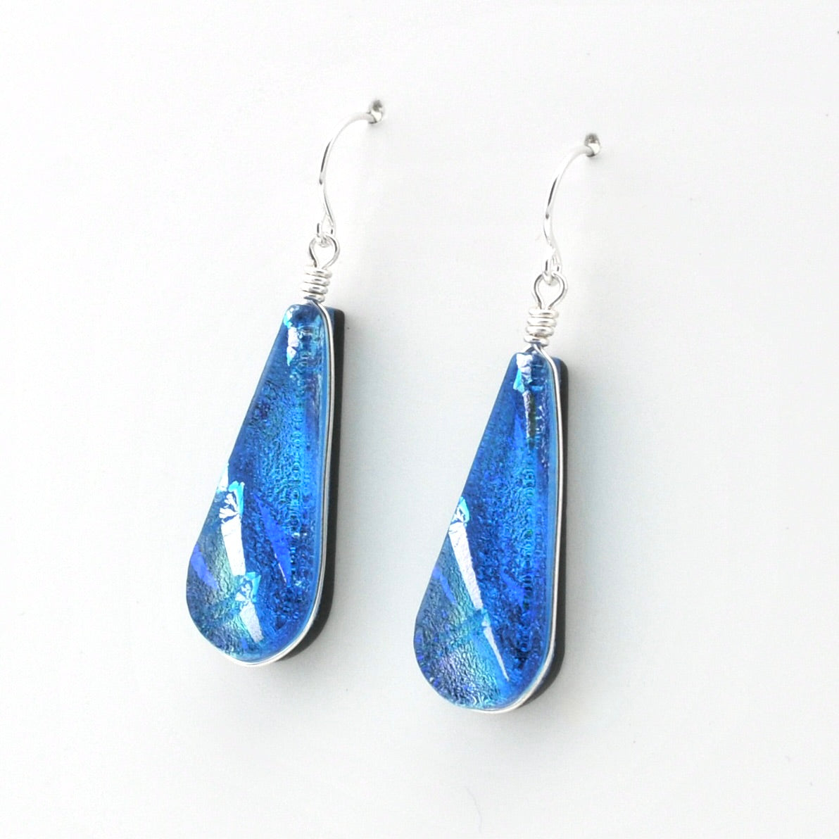 A pair of teardrop-shaped blue glass dangle earrings with silver wire-wrapping and silver fishhook ear wires, shown on a plain white background.