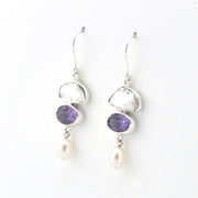 A pair of silver drop earrings featuring a white pearl, a purple amethyst, and a white freshwater pearl dangling below, set against a plain white background.