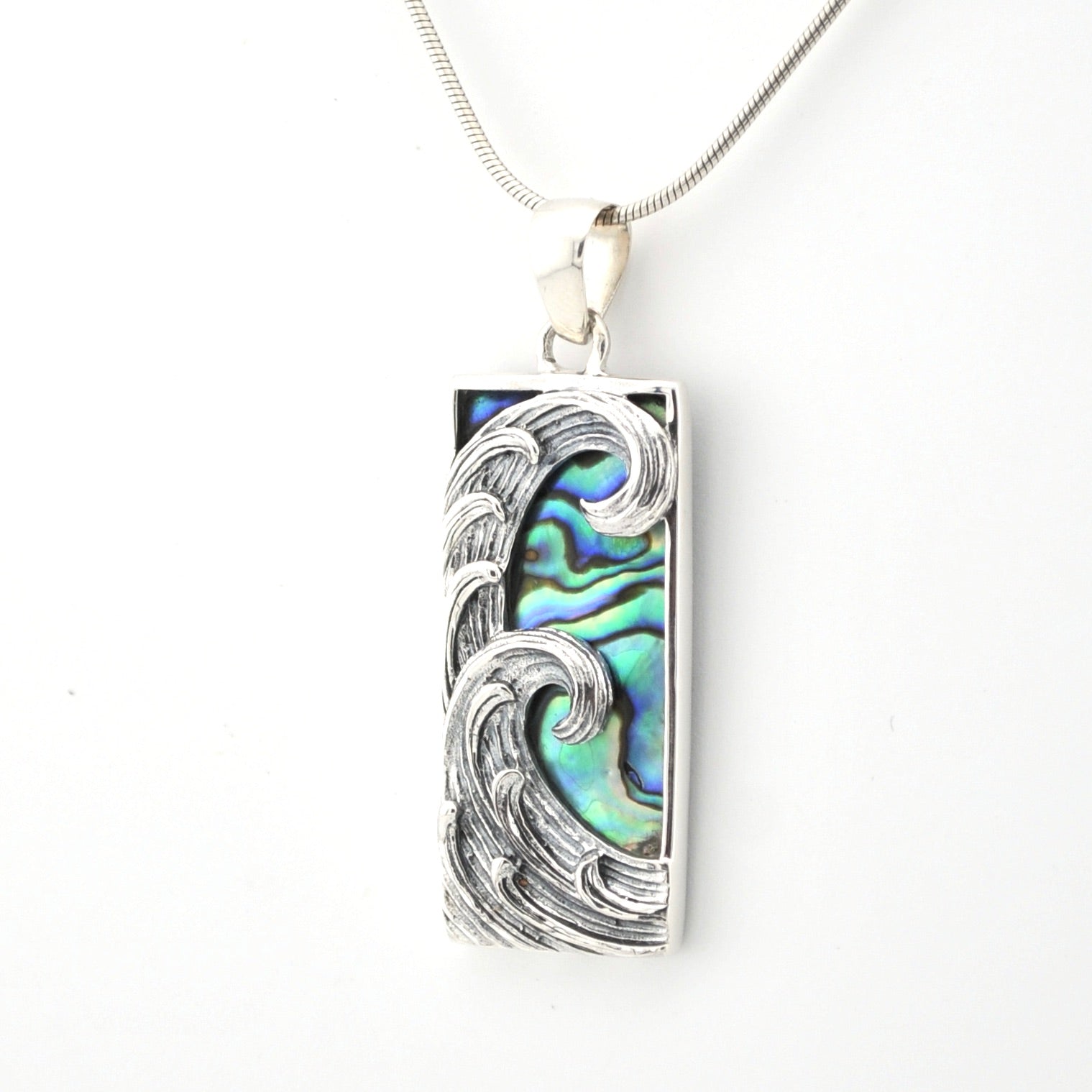 Silver pendant with wave design and abalone shell inlay on a white background