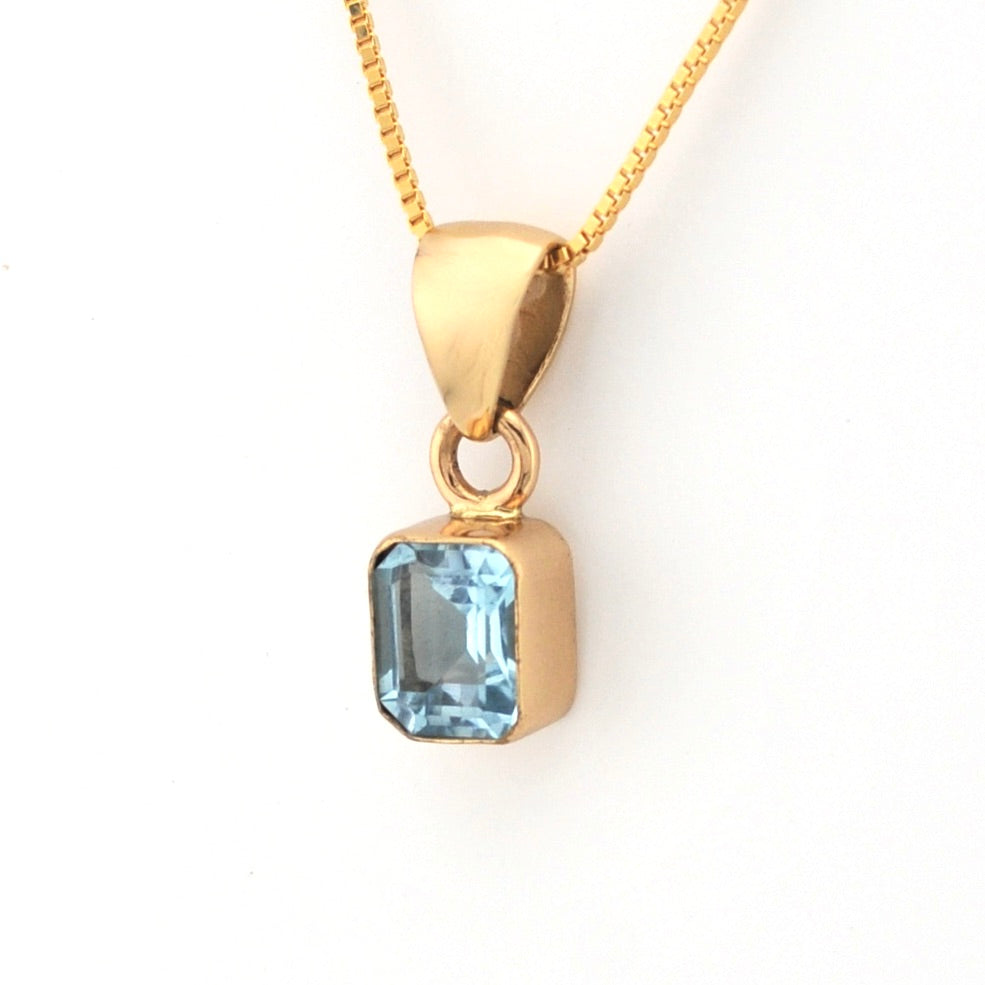 Gold pendant with a blue gemstone on a white background