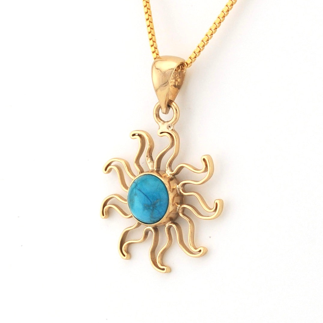 Gold sun-shaped pendant with a blue stone on a white background