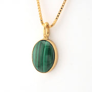 Gold necklace with a green stone pendant on a white background