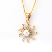 Gold sun-shaped pendant with a pearl center on a white background