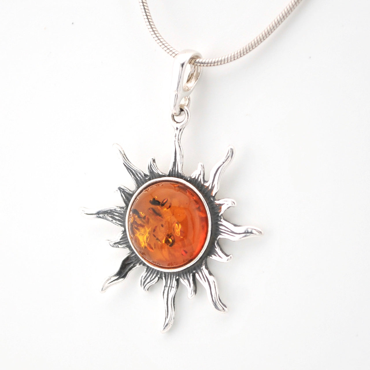 Silver sun-shaped pendant with amber center on a white background