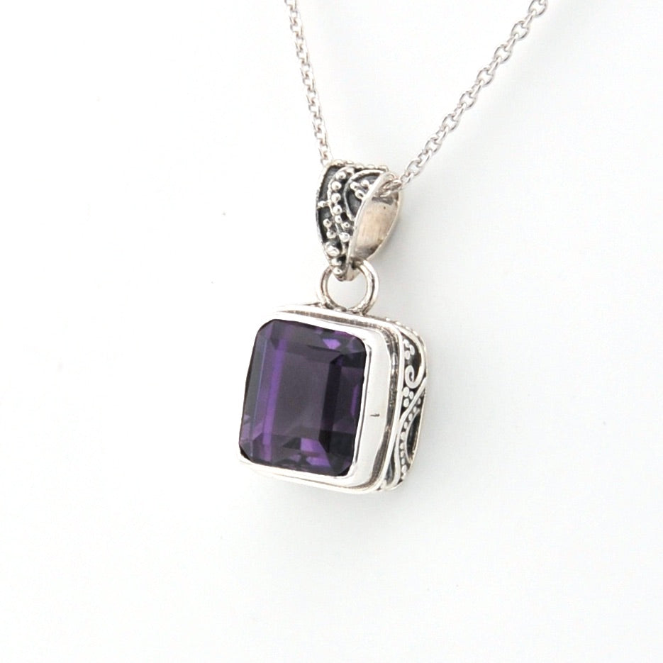Silver pendant with a purple gemstone on a white background