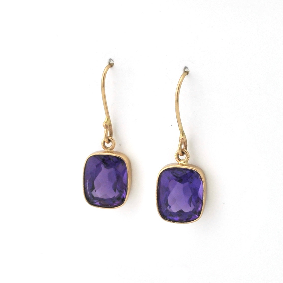 Pair of gold earrings with purple gemstones on a white background