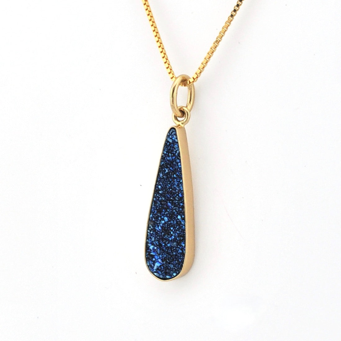 Gold necklace with a blue teardrop pendant on a white background