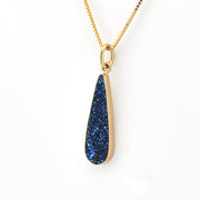 Gold necklace with a blue teardrop pendant on a white background