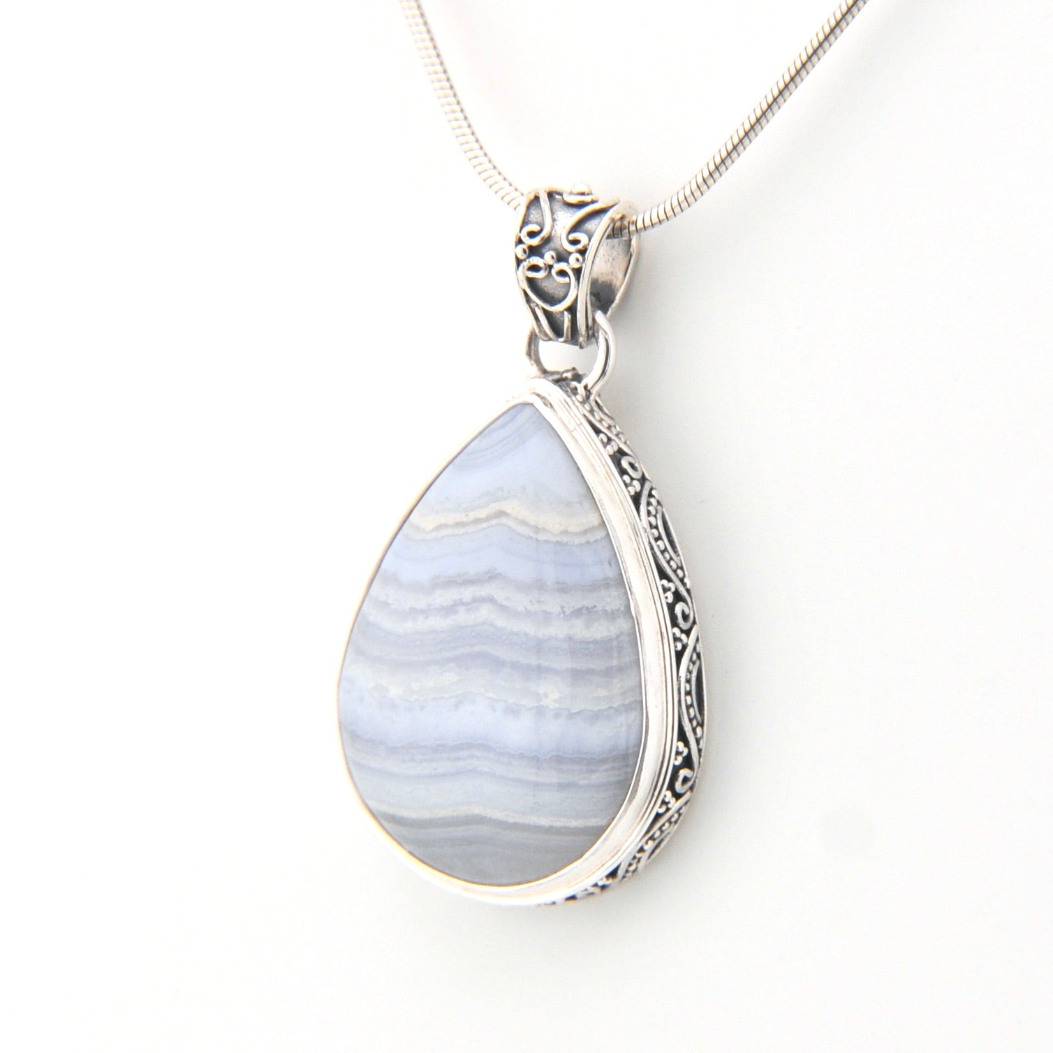 Teardrop-shaped pendant with blue and white pattern on a silver chain against a white background