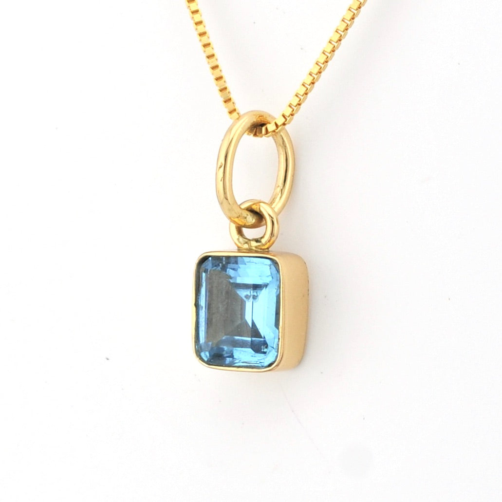 Gold necklace with a blue gemstone pendant on a white background