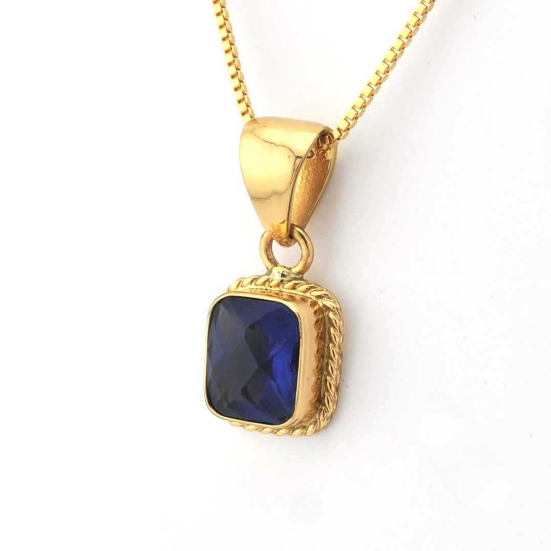 Gold necklace with a blue gemstone pendant on a white background