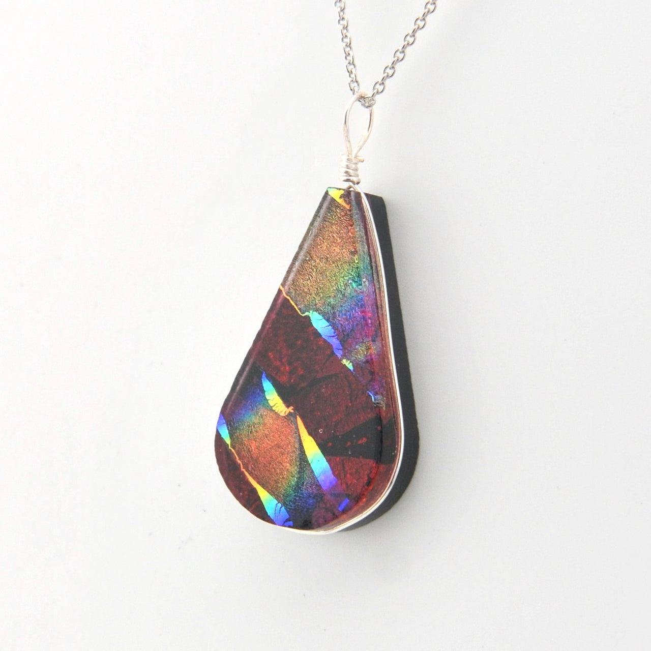 Teardrop-shaped pendant with multicolored iridescent surface on a white background