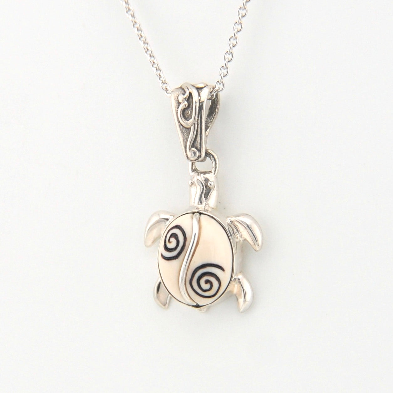 Silver turtle pendant with black spiral design on a white background