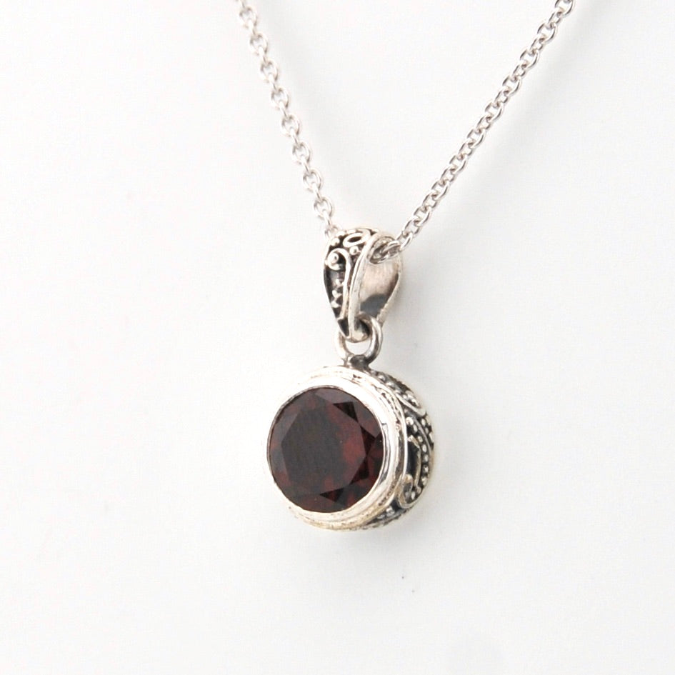 Silver necklace with a round red gemstone pendant on a white background