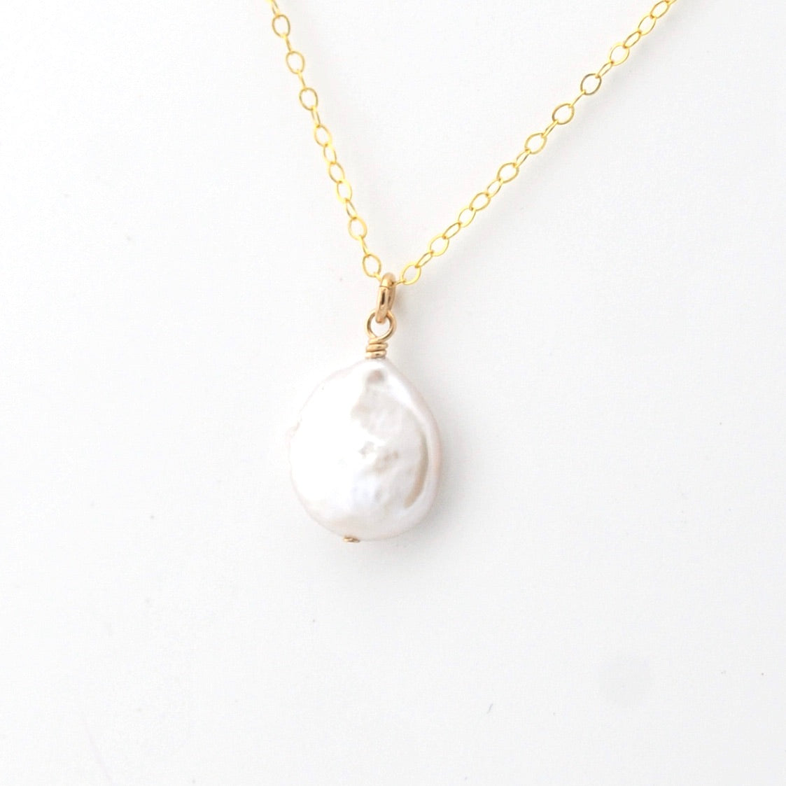 Gold necklace with a white baroque pearl pendant on a white background