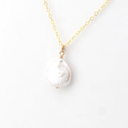 Gold necklace with a white baroque pearl pendant on a white background