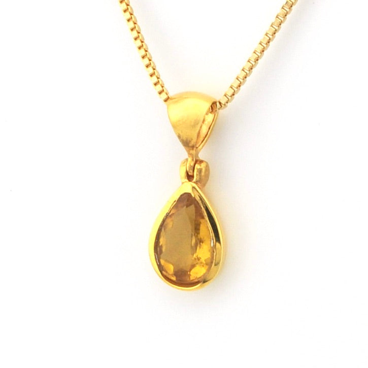 A gold teardrop pendant necklace with a faceted yellow gemstone, suspended from a gold box chain on a white background.