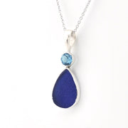 A silver teardrop pendant necklace featuring a large deep blue teardrop stone and a small round light blue gemstone at the top, suspended from a delicate silver chain against a white background.