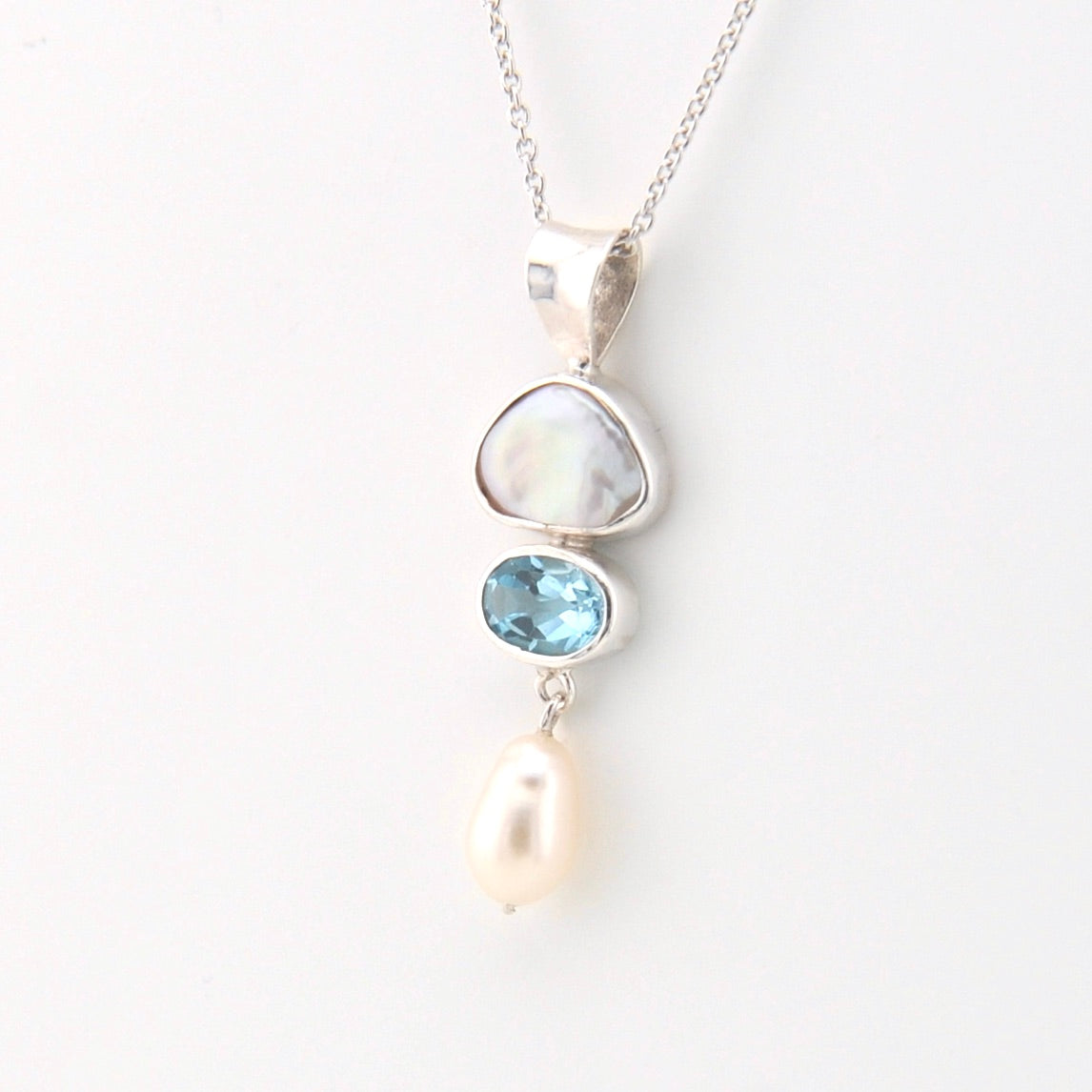 Silver necklace with a pendant featuring a pearl, blue gemstone, and white stone on a light background
