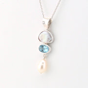 Silver necklace with a pendant featuring a pearl, blue gemstone, and white stone on a light background