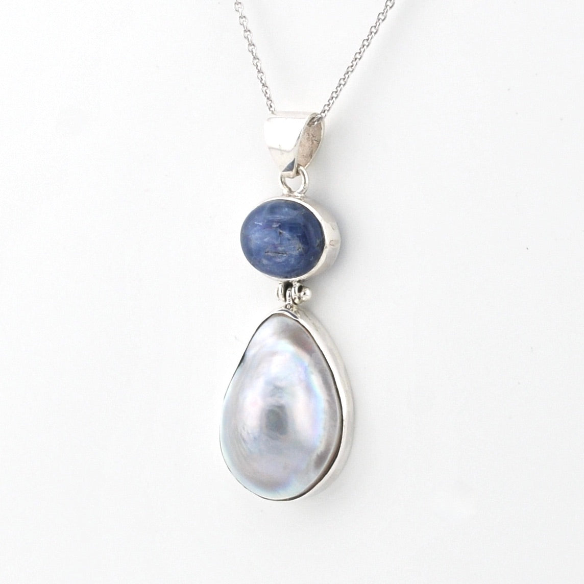 Silver pendant with a teardrop-shaped pearl and blue stone on a white background