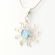 Silver sun-shaped pendant with a blue gemstone on a white background