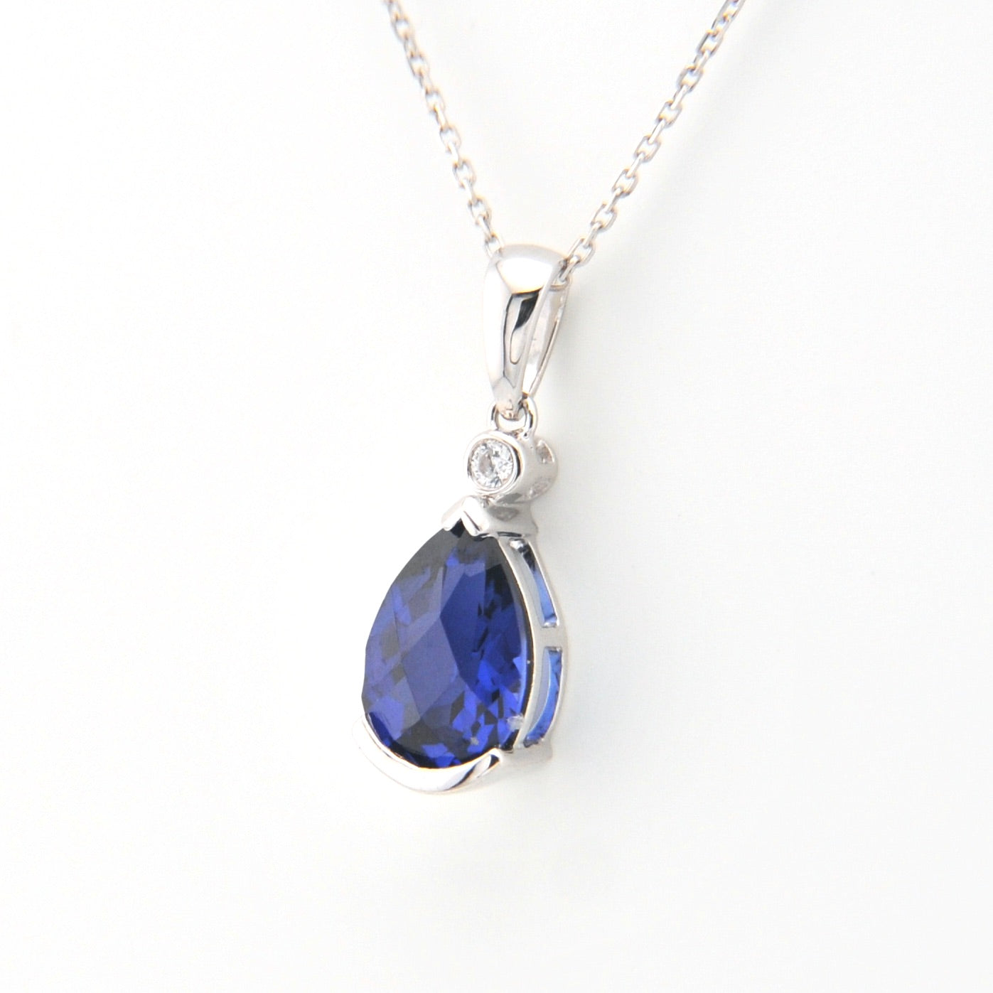 Silver necklace with a blue teardrop pendant on a white background