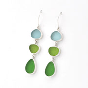 A pair of silver drop earrings featuring three stacked, irregularly shaped sea glass pieces in light blue, lime green, and medium green, shown against a plain white background.