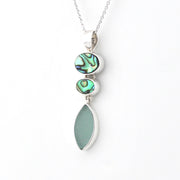 A silver pendant necklace featuring three stacked vertical elements: a large teardrop-shaped light green stone, a smaller oval iridescent abalone shell, and a medium oval abalone shell, suspended from a delicate silver chain on a white background.