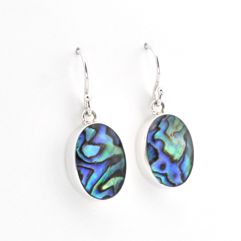 A pair of silver drop earrings featuring oval abalone shell inlays with iridescent blue, green, and purple patterns, set against a plain white background.